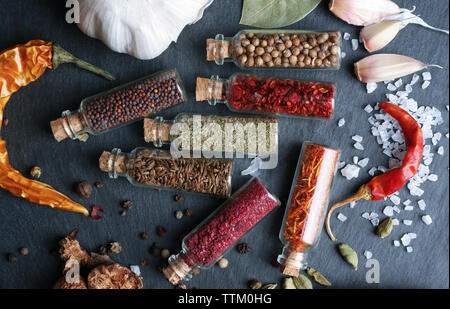 Verschiedene Gewürze in kleinen Glasflaschen auf schwarz Tabelle Stockfoto