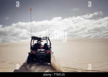 Mann, der Golf Cart auf Sand in der Wüste gegen bewölkter Himmel Stockfoto