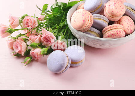 Leckere Makronen mit wunderschönen Rosen auf rosa Hintergrund Stockfoto