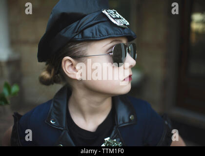 Close-up zuversichtlich, dass Mädchen in der Polizei Kostüm tragen Sonnenbrillen im Stehen gegen Haus während der Halloween Stockfoto