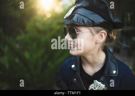 Nahaufnahme der lächelnde Mädchen in Polizei Kostüm tragen Sonnenbrillen im Stehen gegen Pflanzen im Hof während der Halloween Stockfoto