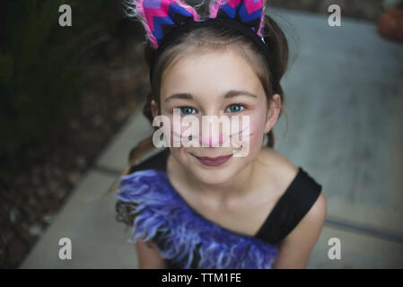 Hohen winkel Portrait von Mädchen mit Gesicht Farbe tragen Halloween Kostüm während der Sitzung in Hof bei Sonnenuntergang Stockfoto