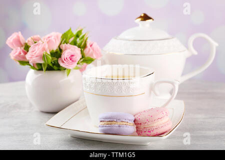 Tasse Tee mit Makronen und Rosen auf hölzernen Tisch Stockfoto