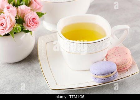 Tasse Tee mit Makronen und Rosen auf hölzernen Tisch Stockfoto