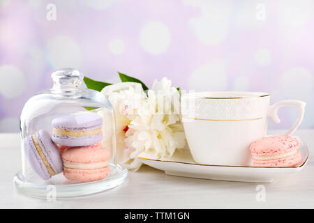 Tasse Tee mit Makronen und Pfingstrosen auf hölzernen Tisch Stockfoto