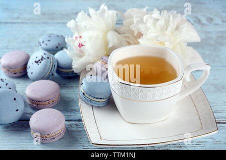 Tasse Tee mit Makronen und Pfingstrosen auf hölzernen Tisch Stockfoto