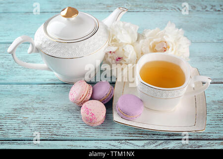 Tasse Tee mit Makronen und Pfingstrosen auf hölzernen Tisch Stockfoto