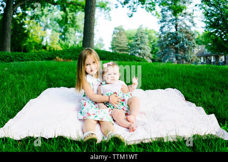 Porträt von zwei Schwestern sitzen auf einer Decke auf grünem Gras Stockfoto