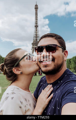 Portrait von liebevolle Freundin küssen Lächeln Freund gegen Eiffelturm in Stadt Stockfoto