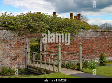 Kleine Holzbrücke mit einer interessanten offenen Muster kreuzt ein Bach und führt in einem ummauerten Garten. Stockfoto