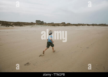 Ansicht der Rückseite des Jungen, die auf Sand am Strand gegen bewölkter Himmel Stockfoto