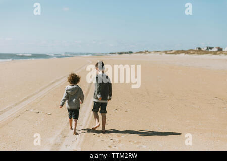 Ansicht der Rückseite des Brüder gehen auf Sand am Strand gegen Himmel während der sonnigen Tag Stockfoto