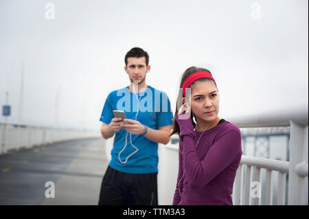 Zuversichtlich weiblichen Athleten mit Ohrhörer beim Stehen mit Freund auf die Bay Bridge Stockfoto