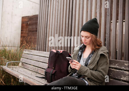 Junge Frau mit Smart Phone beim Sitzen auf der Werkbank Stockfoto