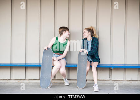 Teenage Freunde mit skateboards sprechen beim Sitzen auf der Bank gegen die Wand Stockfoto
