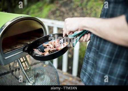 Mittelteil des Menschen, Pfanne mit Speck im Backofen auf der Veranda Stockfoto