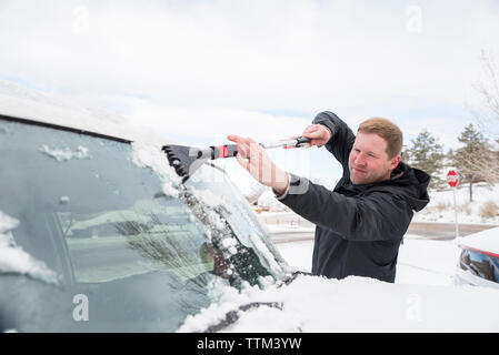 Mann Reinigung Schnee vom Auto Windschutzscheibe im Winter Stockfoto