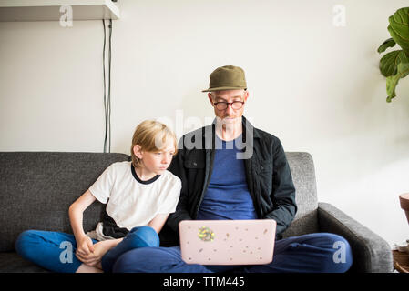 Sohn auf Laptop von Vater beim Sitzen auf einem Sofa gegen die Wand im Wohnzimmer verwendet werden Stockfoto