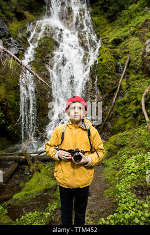 Junge hält Kamera beim Stehen gegen Wasserfall im Olympic National Park Stockfoto