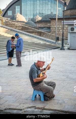 Älterer Mann spielt Musik auf einem massivem Messing Saiteninstrument, ausserhalb in den alten Basar von Skopje sitzen. Stockfoto