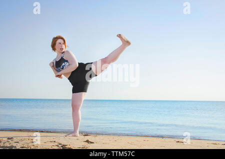 Frau üben Kickboxen am Strand gegen den klaren Himmel Stockfoto