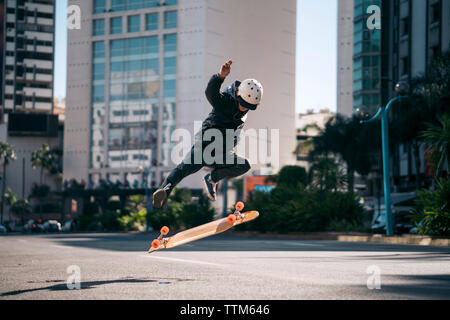 Mann Durchführung stunt während Skateboarding auf der Straße in der Stadt Stockfoto