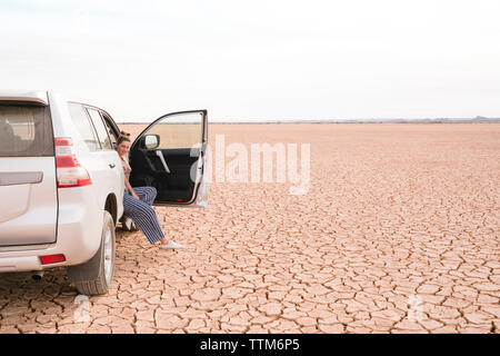 Portrait von Frau sitzt im Off-road-Fahrzeug in der Wüste gegen Sky Stockfoto