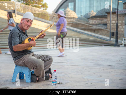 Älterer Mann spielt Musik auf einem massivem Messing Saiteninstrument, ausserhalb in den alten Basar von Skopje sitzen. Stockfoto