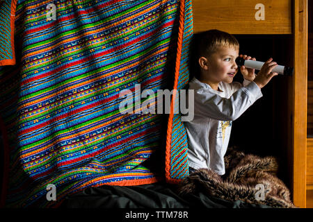 Neugierige junge Schauen durch Teleskop während auf ständigen Etagenbett Stockfoto