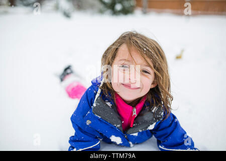 Portrait von niedlichen Mädchen liegt auf schneebedeckten Feld Stockfoto