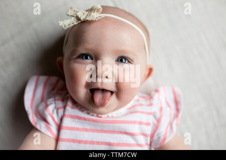 Close-up Portrait von Happy Baby girl Zunge heraus, während sie sich auf dem Bett zu Hause. Stockfoto