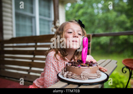 Mädchen bläst Nummer 6 Kerze zum Geburtstag Kuchen in der Veranda Stockfoto