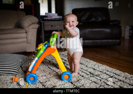 Portrait von Happy Baby Mädchen mit Walker stehen auf Teppich zu Hause Stockfoto