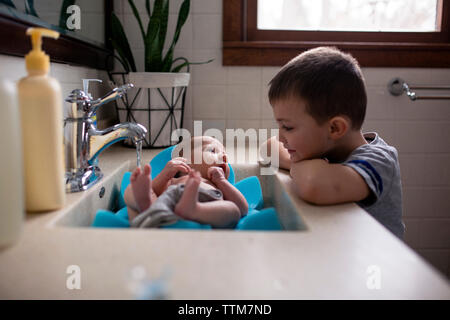 Bruder auf der Suche nach baby boy in Waschbecken im Bad zu Hause Stockfoto