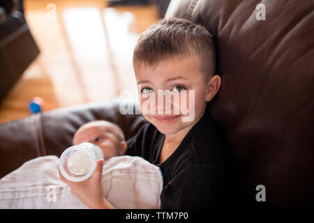 Porträt der jungen Fütterung Milch zu seinem Bruder von baby Flasche beim Sitzen auf dem Sofa zu Hause Stockfoto