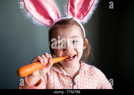 Portrait von verspielten Mädchen mit Hasenohren Stirnband beim Beißen Karotte zu Hause Stockfoto