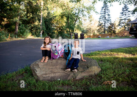 Bruder und Schwester Geschwister sitzen warten auf Rock For School Bus Stockfoto