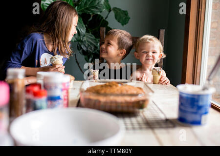 Drei Geschwister genießen Sie frisch gebackene süße Leckereien, dumm Stockfoto