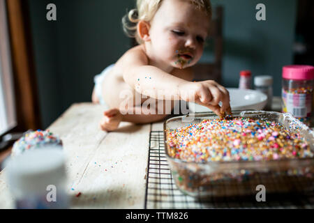 Kleinkind Mädchen schleichen bunten Streuseln aus der frisch gebackenen Kuchen Stockfoto