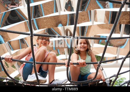 Low Angle Portrait von sorglosen lächelnde Schwestern hockend auf Seilen und Spielplatz spielen Stockfoto