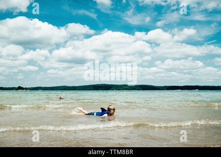 Junger Mann, Schwimmbrille, während im Meer gegen bewölkter Himmel liegend Stockfoto