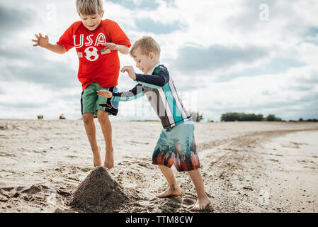 Gerne Brüder spielen mit Sand am Strand gegen bewölkter Himmel Stockfoto