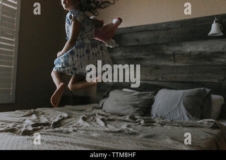 Fröhliches Mädchen springen auf Bett zu Hause Stockfoto