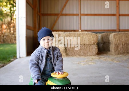 Portrait von Baby Junge sitzt auf spielzeugauto in der Scheune Stockfoto