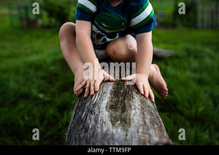Untere Partie der Junge sitzt auf Log in Hinterhof Stockfoto