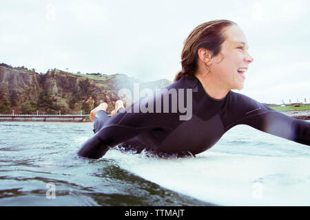 Glückliche Frau liegend auf Surfbrett im Meer gegen Sky Stockfoto