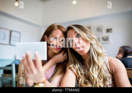 Weibliche Freunde Gesichter machen während der Einnahme von selfie durch Smart Phone im Cafe Stockfoto