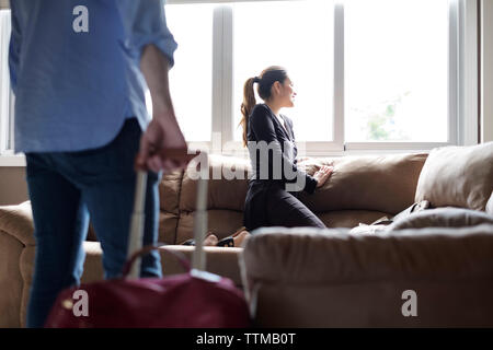 Lächelnd Freundin suchen zwar Fenster, während Freund holding Gepäck im Vordergrund Rental House Stockfoto