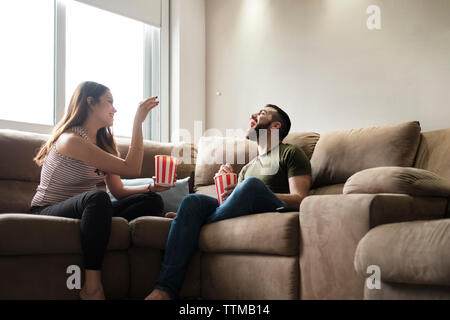 Verspielte Freundin werfen Popcorn im Mund, während der Freund sitzt auf einem Sofa in vermietung haus Stockfoto