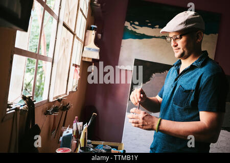 Mitte der erwachsenen männlichen kubanischen Künstlerin mischen malen Mit Pinsel in seiner Werkstatt Stockfoto